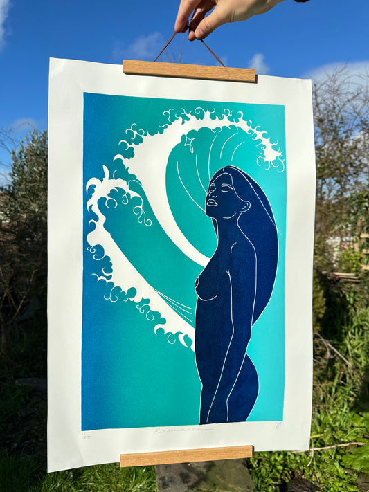 Framed artwork of a stylized figure with a wave, held outdoors.